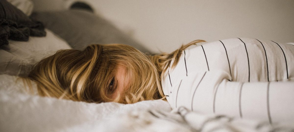 How Many Hours Of Sleep Should You Be Getting Each Night? Woman looking tired on a bed.