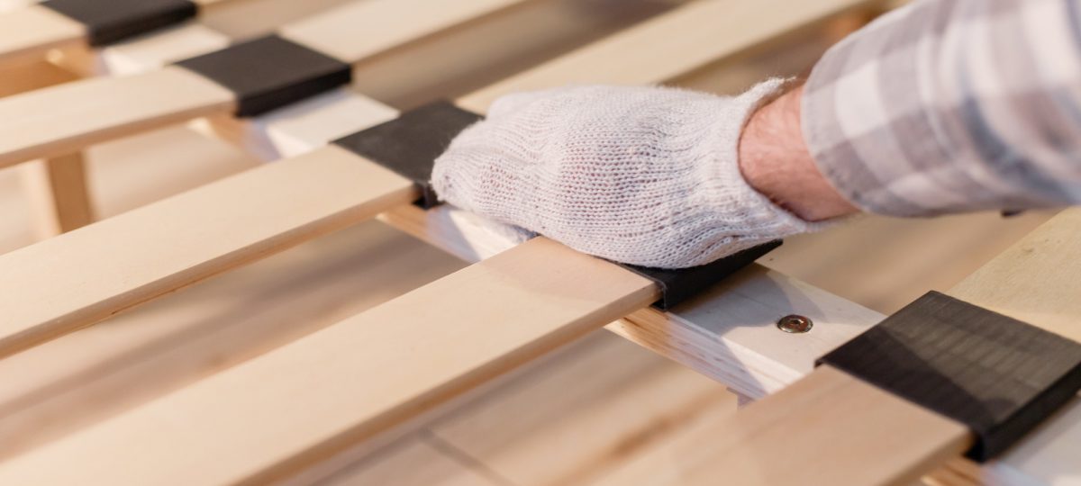 Male worker's hand in glove assembling bed, connecting slats to bed frame. Frames or boxsprings?