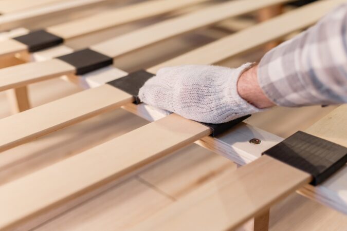 Male worker's hand in glove assembling bed, connecting slats to bed frame. Frames or boxsprings?