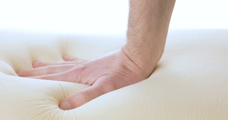 Hand is pressing a memory foam mattress. Learn all about foam mattresses.