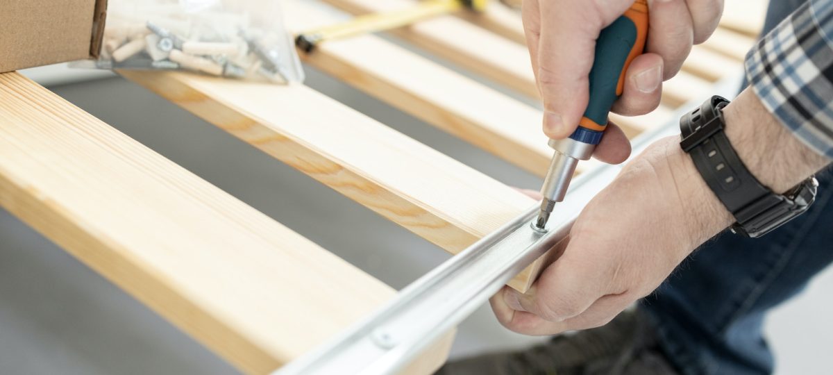 Close up of hands assembling a split box spring with a screwdriver.