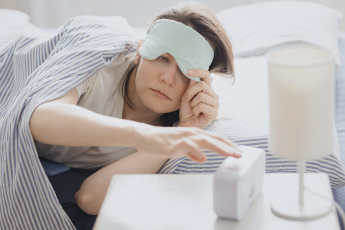 Woman in bed with a sleep mask wakes up and turns off the alarm. a clock with a timer, a woman yawns.