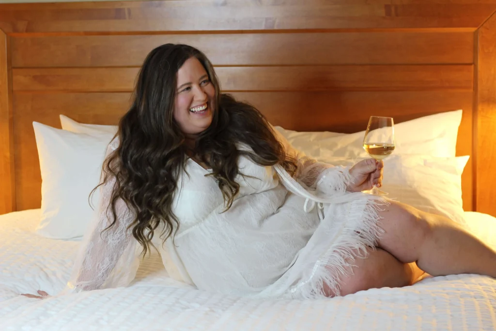 A plus sized woman smiling and drinking wine on a bed. Heavy Duty Mattress Vs. Standard Foundation.