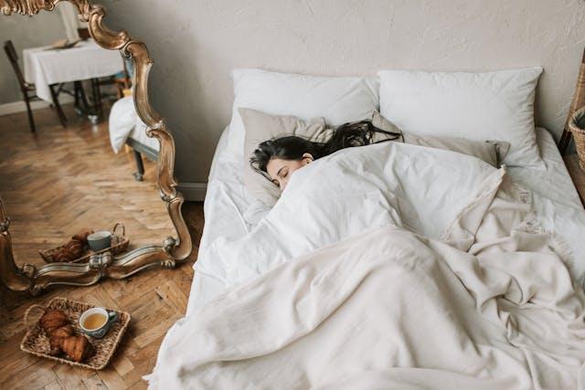Woman sleeping in her bed, with a mirror and a breakfast near the bed.