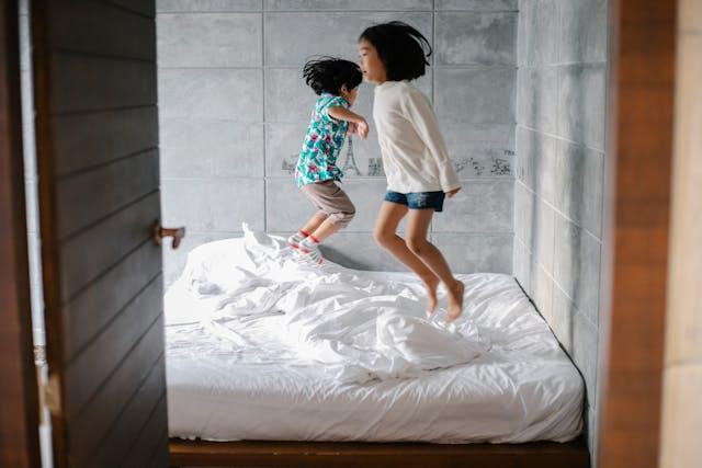 Two kids jumping on bed.